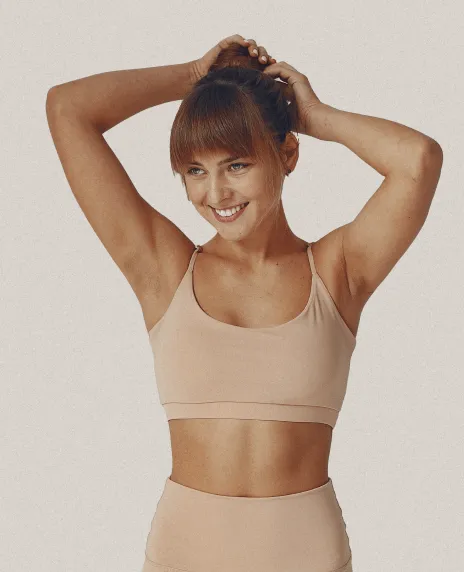 Mujer sonriente en ropa deportiva acomodándose el cabello con las dos manos.